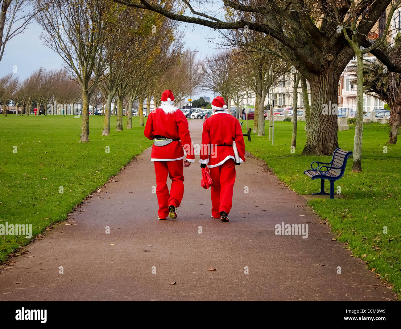 Two men dressed as Santa walk home through a park Stock Photo