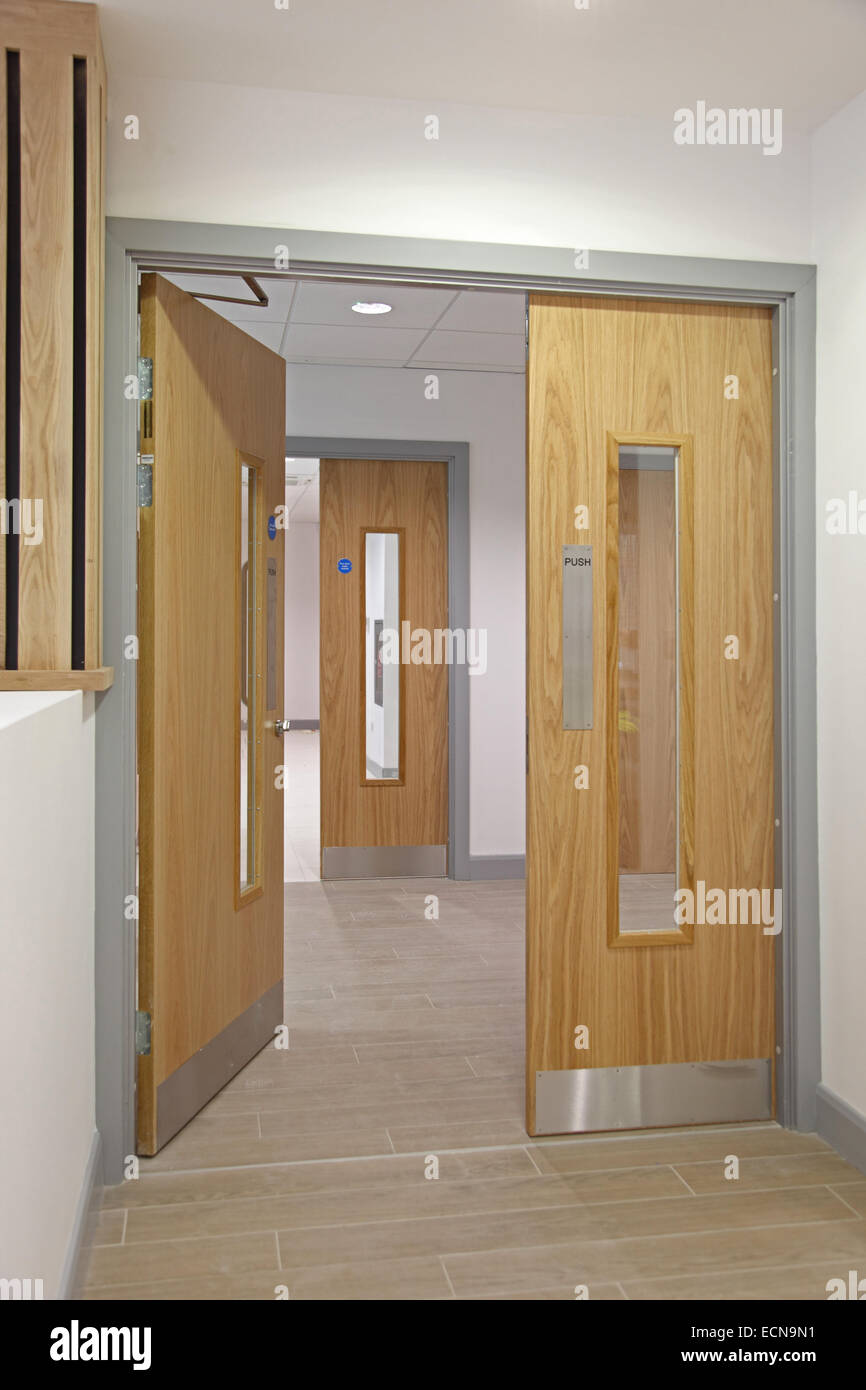 A modern London office corridor showing oak-finish double fire doors leading to the stair well. One door partially open. Stock Photo