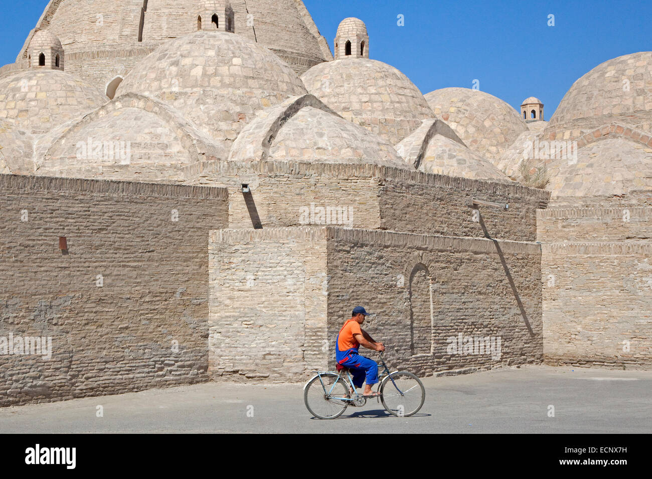 Uzbek man cycling in front of mosque in the ancient historic city of Bukhara / Buxoro, Uzbekistan Stock Photo