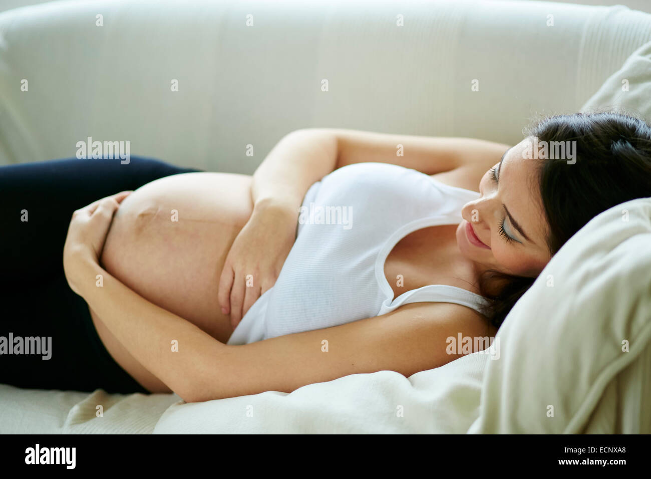 Pregnant woman sat relaxing on sofa Stock Photo