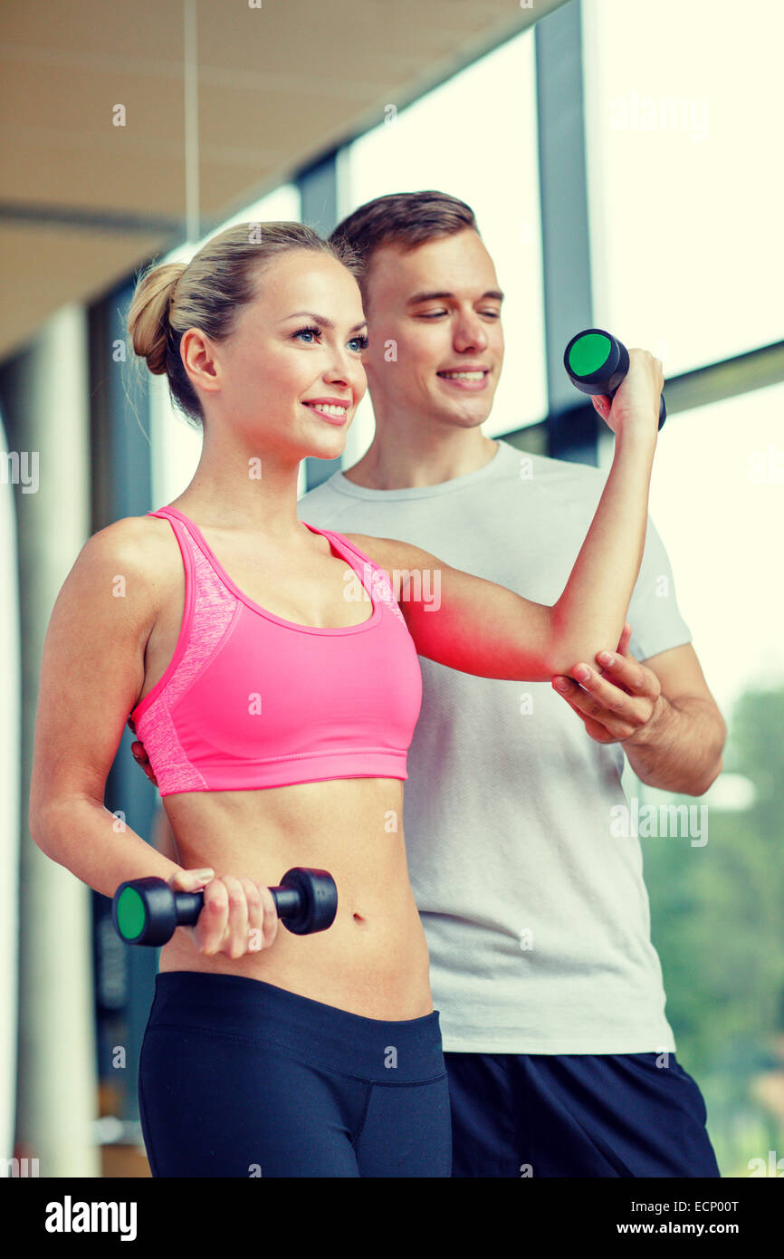 smiling young woman with personal trainer in gym Stock Photo