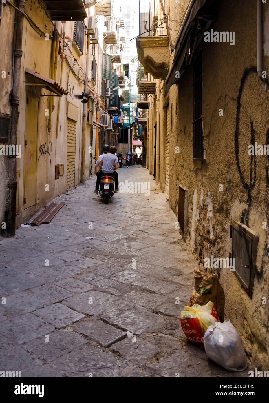 PALERMO, SICILY, ITALY - OCTOBER 3, 2012: Two unidentified men on a moped circulate through a narrow alley in which there are tr Stock Photo