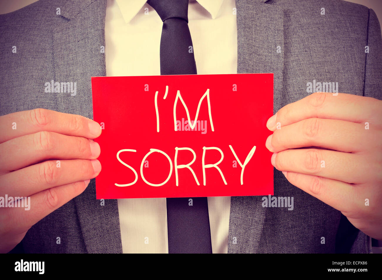 a young man showing a red signboard with the text I am sorry written in it Stock Photo