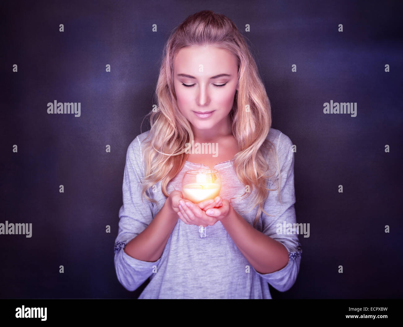 Attractive woman with candle on dark background, calm girl with closed eyes praying, Christmas holidays concept Stock Photo