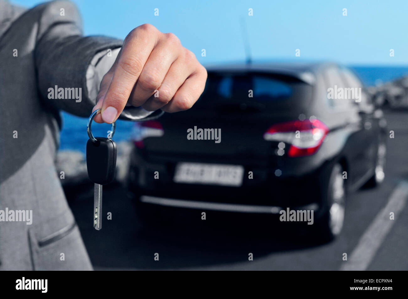a man in a gray suit offering a car key to the observer, with a car in the background Stock Photo