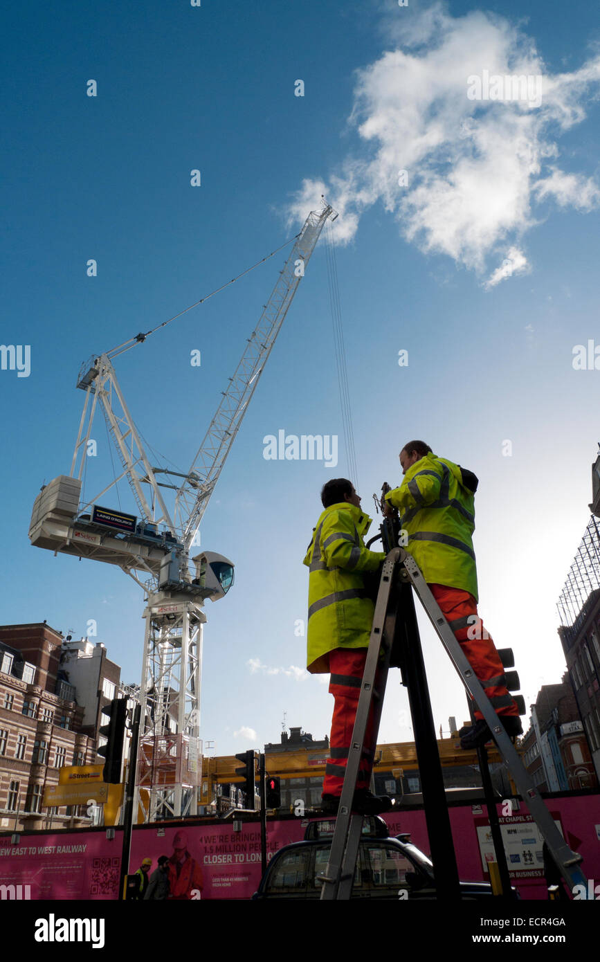 Two workmen stand on ladders working on lights and crane on