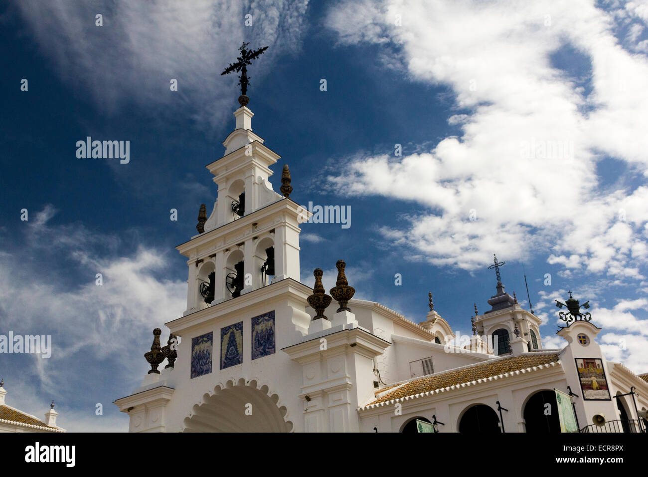 Bell Tower, Crucifix and Roof Detail of the Hermitage of El Rocío against a vivid Blue Sky with Light Cloud. Donana Park, Spain. Stock Photo