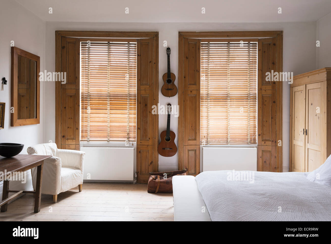 Classical guitars hung up on wall of bedroom with pine window shutters and white armchair Stock Photo