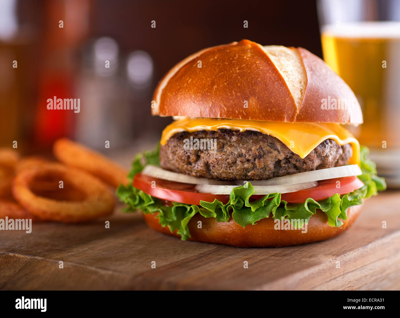A delicious gourmet cheeseburger on a pretzel bun with lettuce, onion, and tomato. Stock Photo