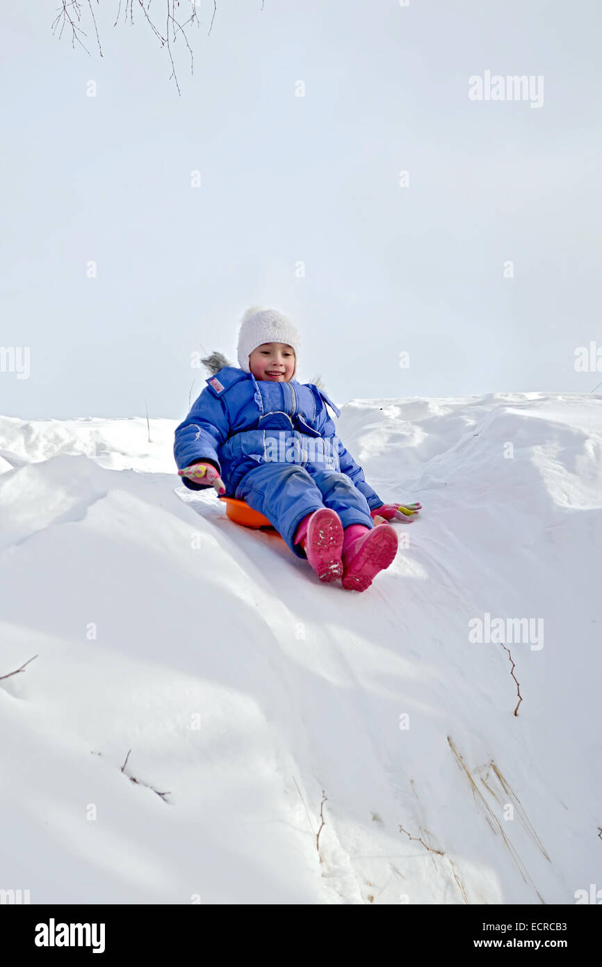 Little girl on a sled sliding down a hill on snow in winter Stock Photo
