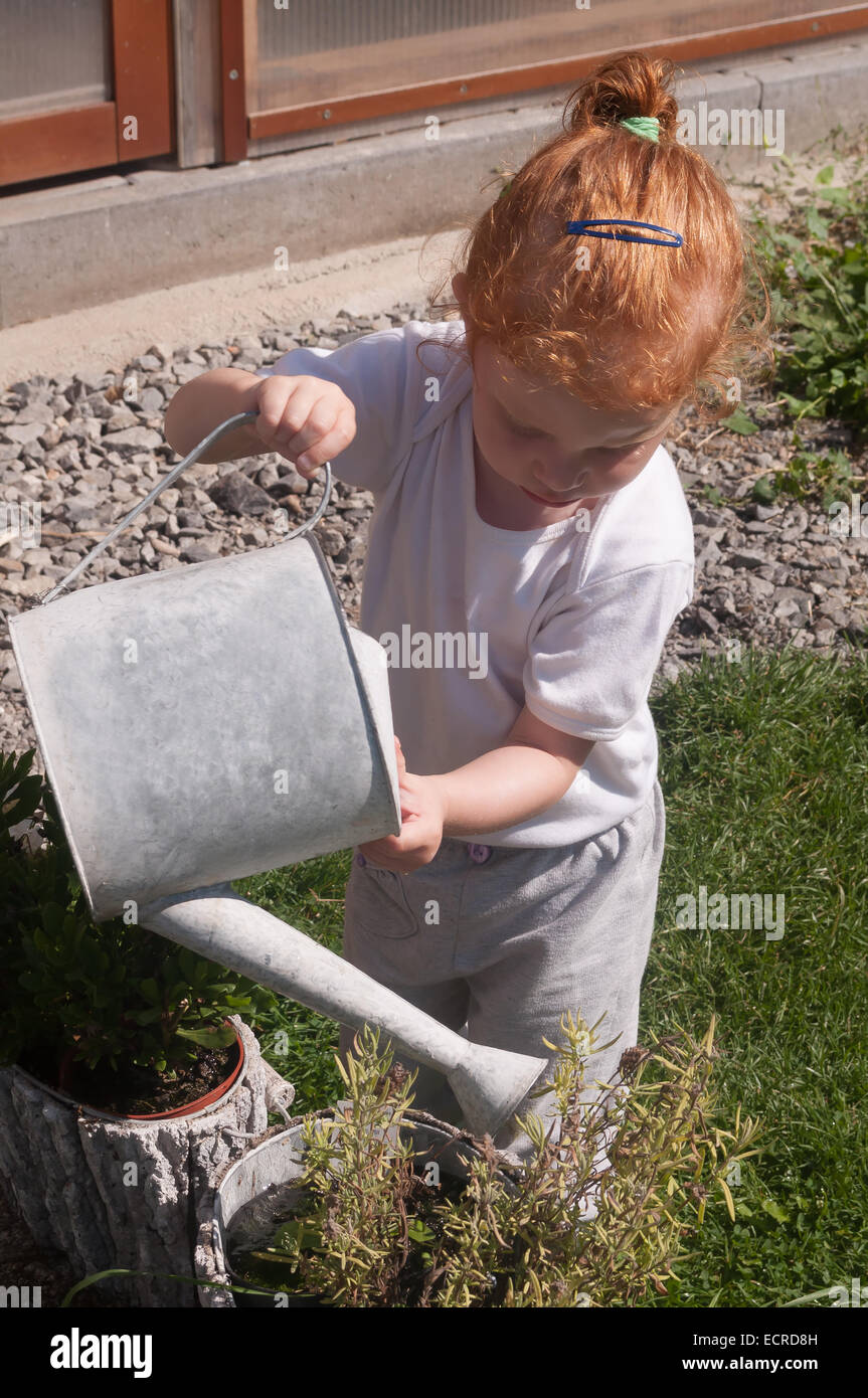 Little girl watering the flowers in the pot with watering can Stock Photo