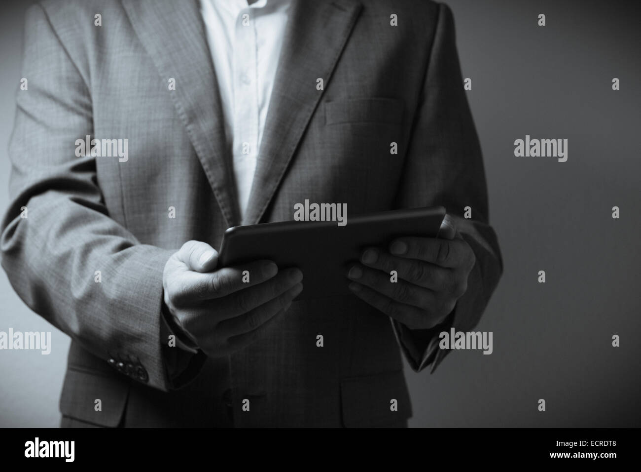 The image displays an individual dressed in a suit holding a tablet computer. Only the person's neck to waist is visible in the Stock Photo