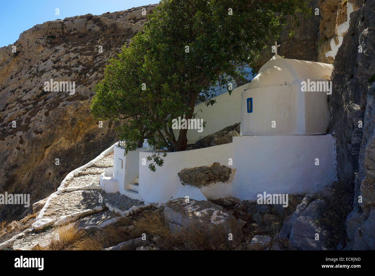 White painted chapel under cliff face with trees and sunlit steps Stock Photo