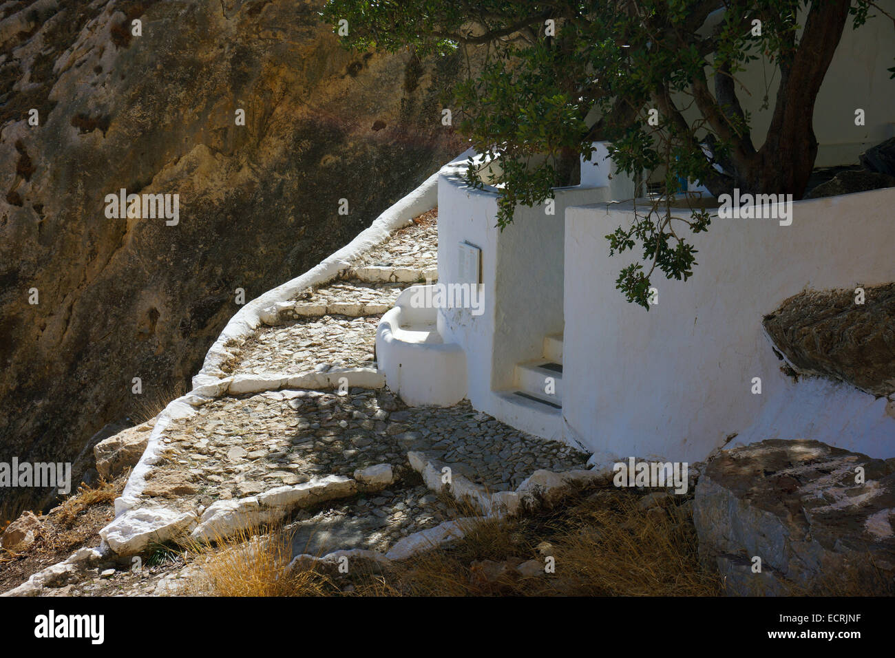 White painted chapel wall under cliff face with sunlit steps trees Stock Photo