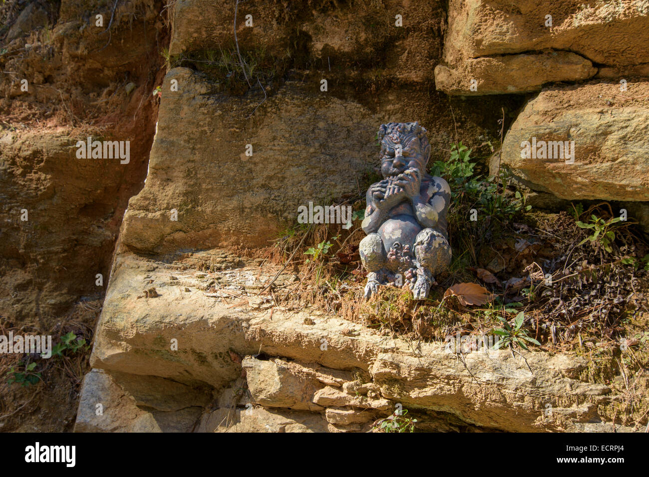 Garden statue of Pan playing flute sitting on rock ledge Stock Photo