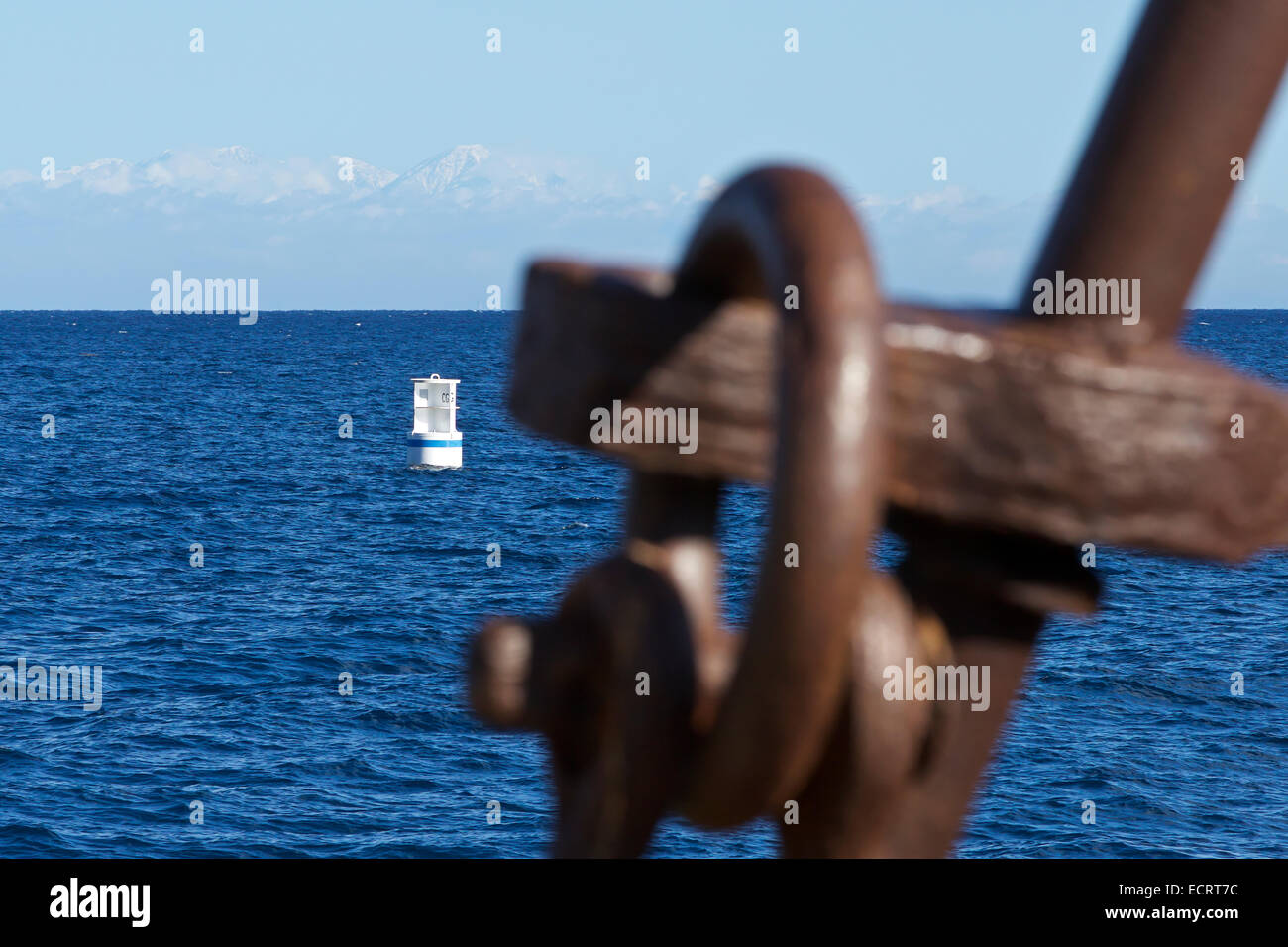 Fresh Snow On The San Gabriel Mountains Viewed From Avalon, Catalina Island, California. A Rusting Ships Anchor Blurred In The Foreground. Stock Photo
