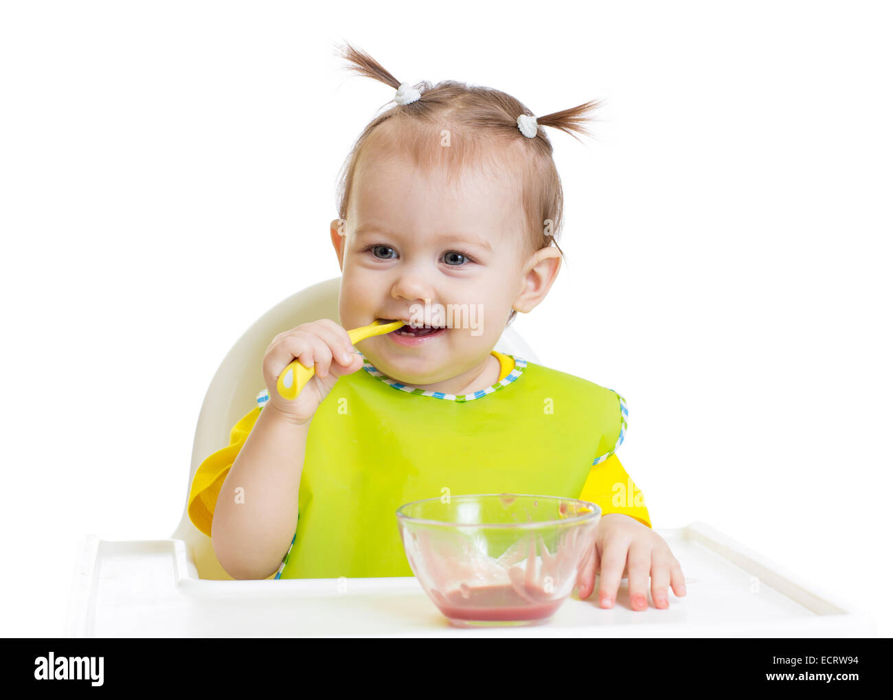 Baby eating with spoon sitting at table isolated Stock Photo