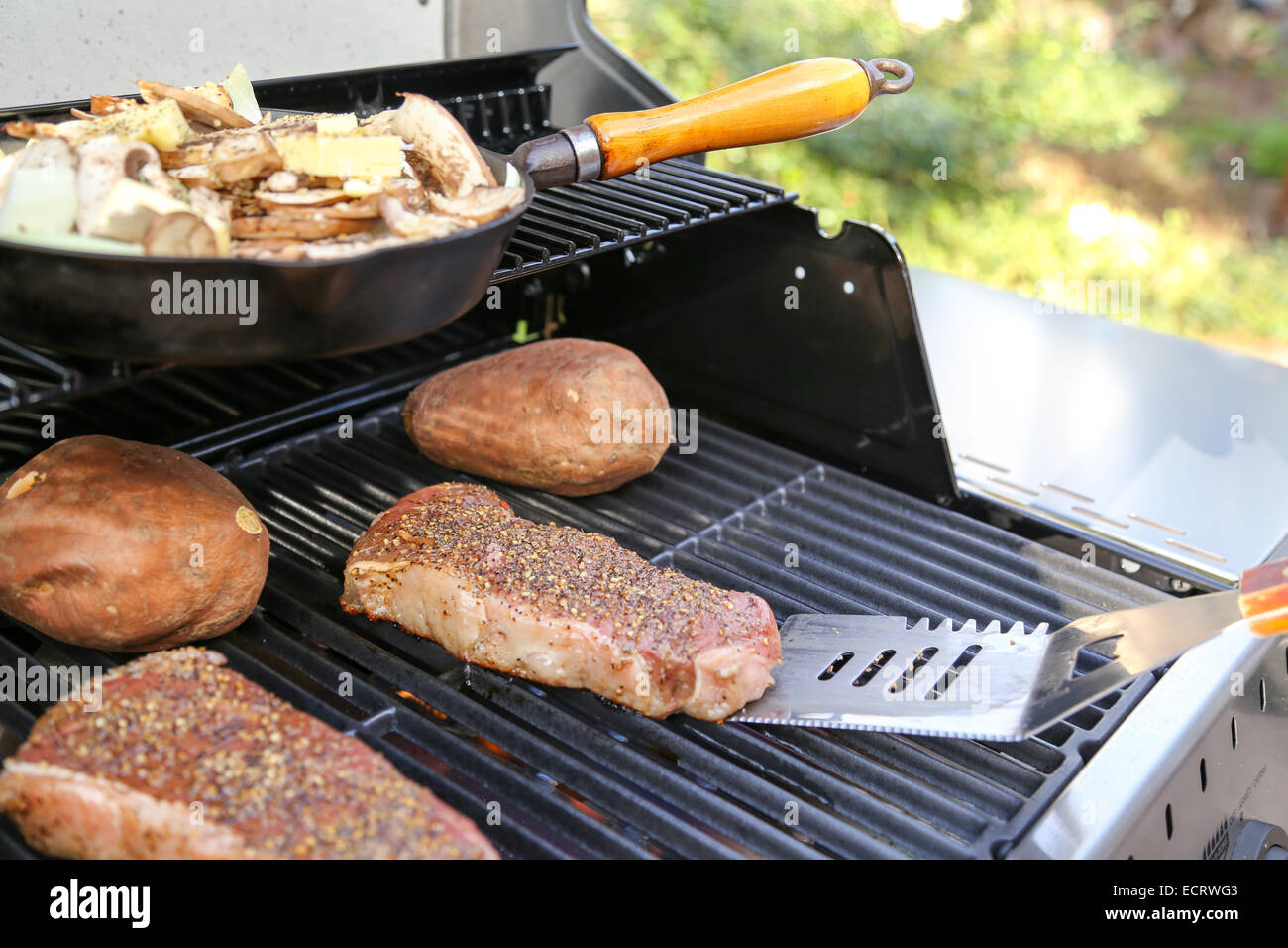A perfect summer BBQ dinner under way on the grill, including steaks, sweet potatoes and a