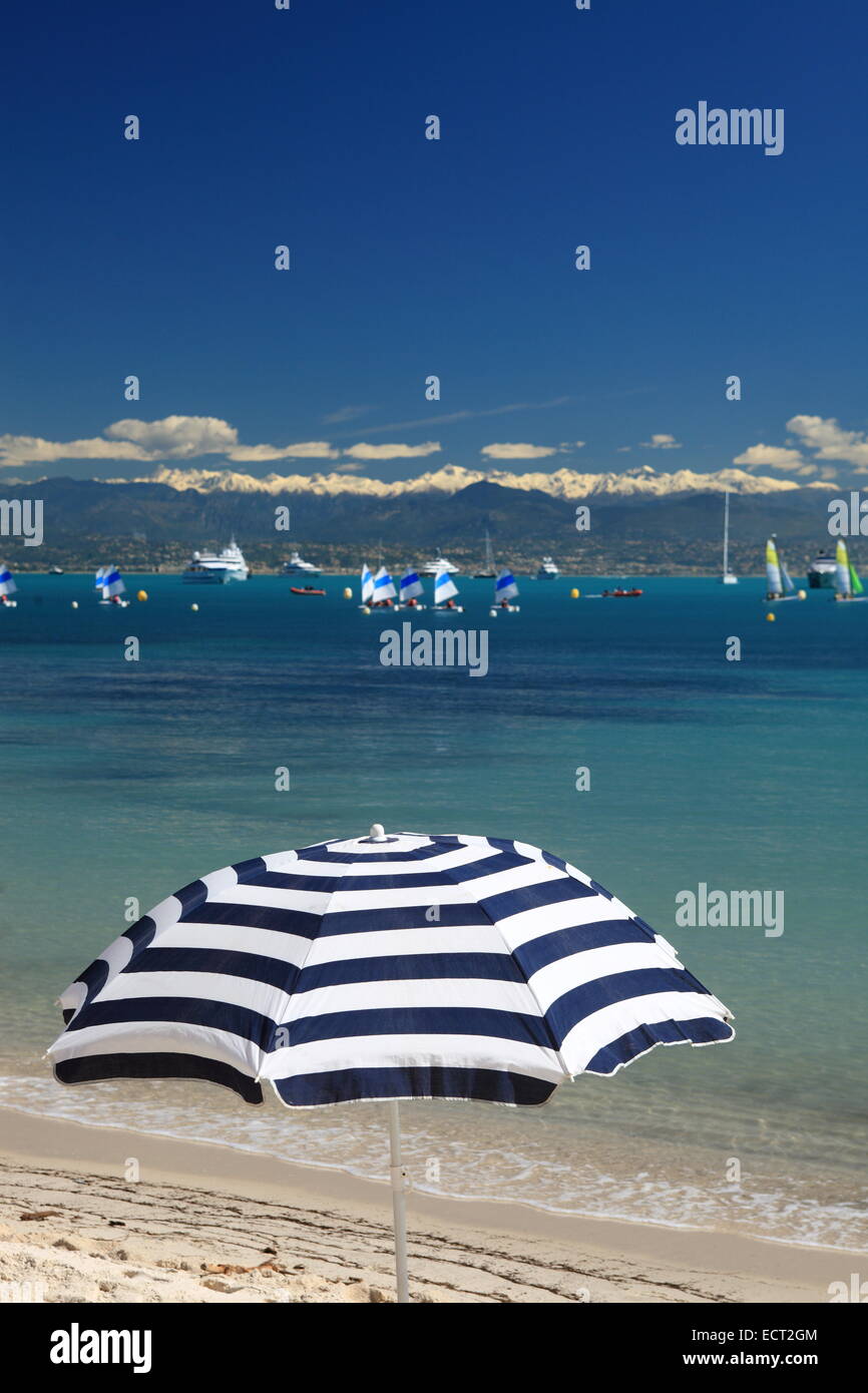 White and blue stripes sunshade with the beautiful view of Antibes with the Mercantour snowed mountain summit in the background. Stock Photo