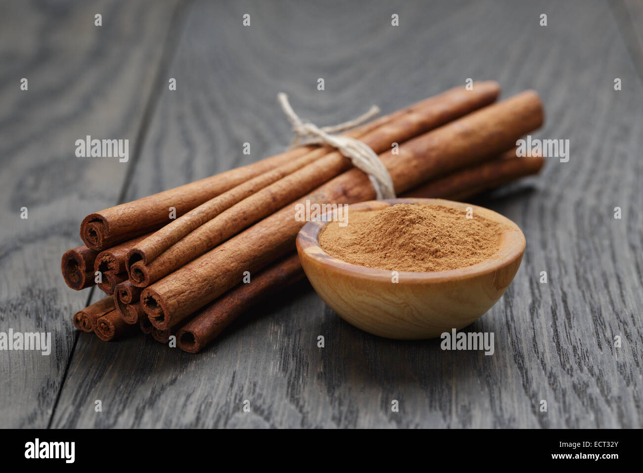 bunch of cinnamon sticks tied with twine and powder in bowl, on rustic ...