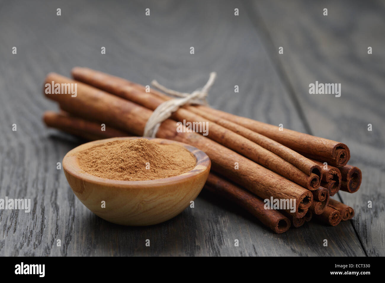 bunch of cinnamon sticks tied with twine and powder in bowl, on rustic ...