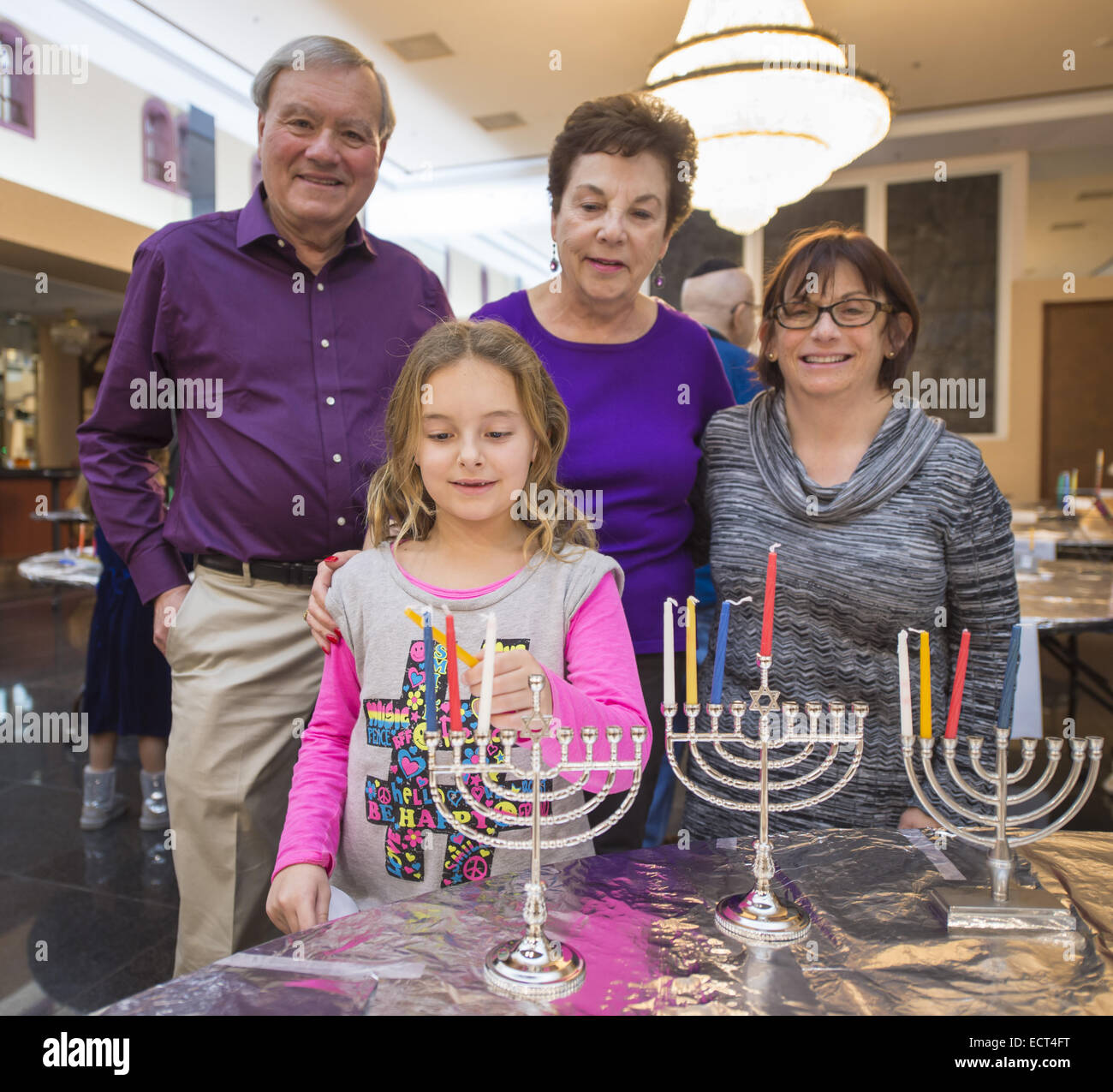 Merrick, New York, USA. 18th Dec, 2014. Granddaughter EMILY MIKOLA, 8, her Grandpa and Grandma BLOOMFIELD, and (at far right) their friend MARCI SILVERMAN, each get a menorah ready when the Merrick Jewish Centre attemps to regain the Guinness World's Record for Most Menorot Lit in One Place at One Time that the congregation held in 2011. On the third night of Hanukkah, the 'Light Up the Night 2 - Bringing the Record Home' event also included a ceremonial candle lighting in the main santuary. Though the Menorah Lighing goal to light at least 1,000 menorot was missed, and the record w Stock Photo