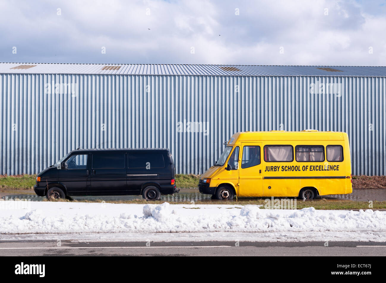 Isle of Man - Jurby School of Excellence - old mini bus parked in a large puddle Stock Photo