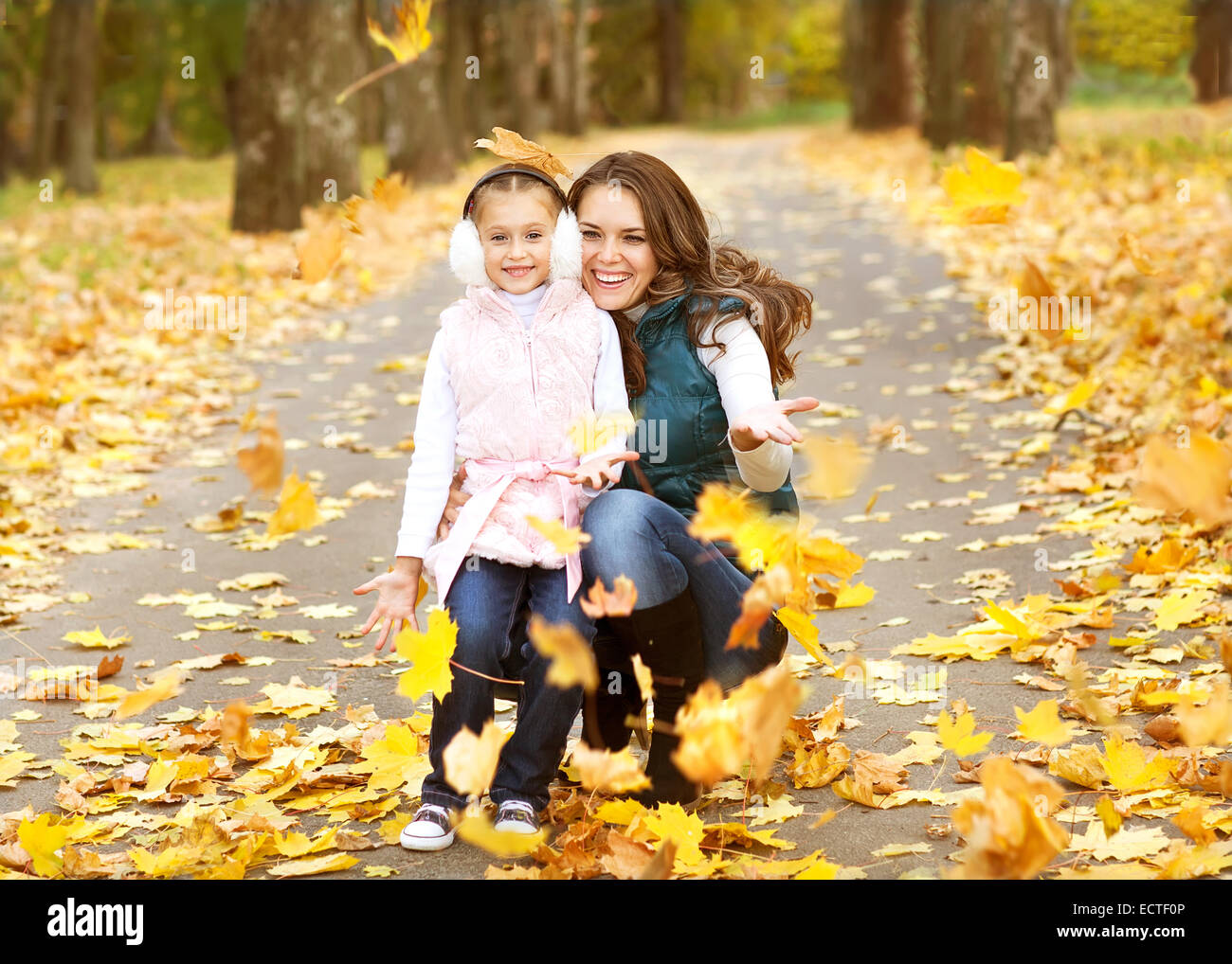 Mother and daughter having fun in the autumn park among the falling ...