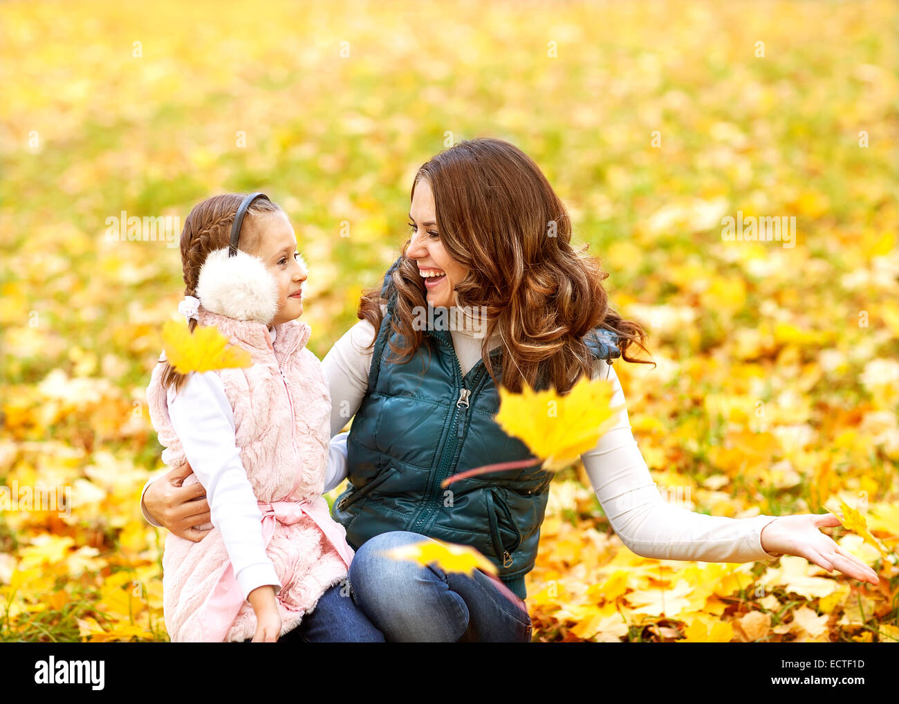Mother and daughter having fun in the autumn park among the falling ...