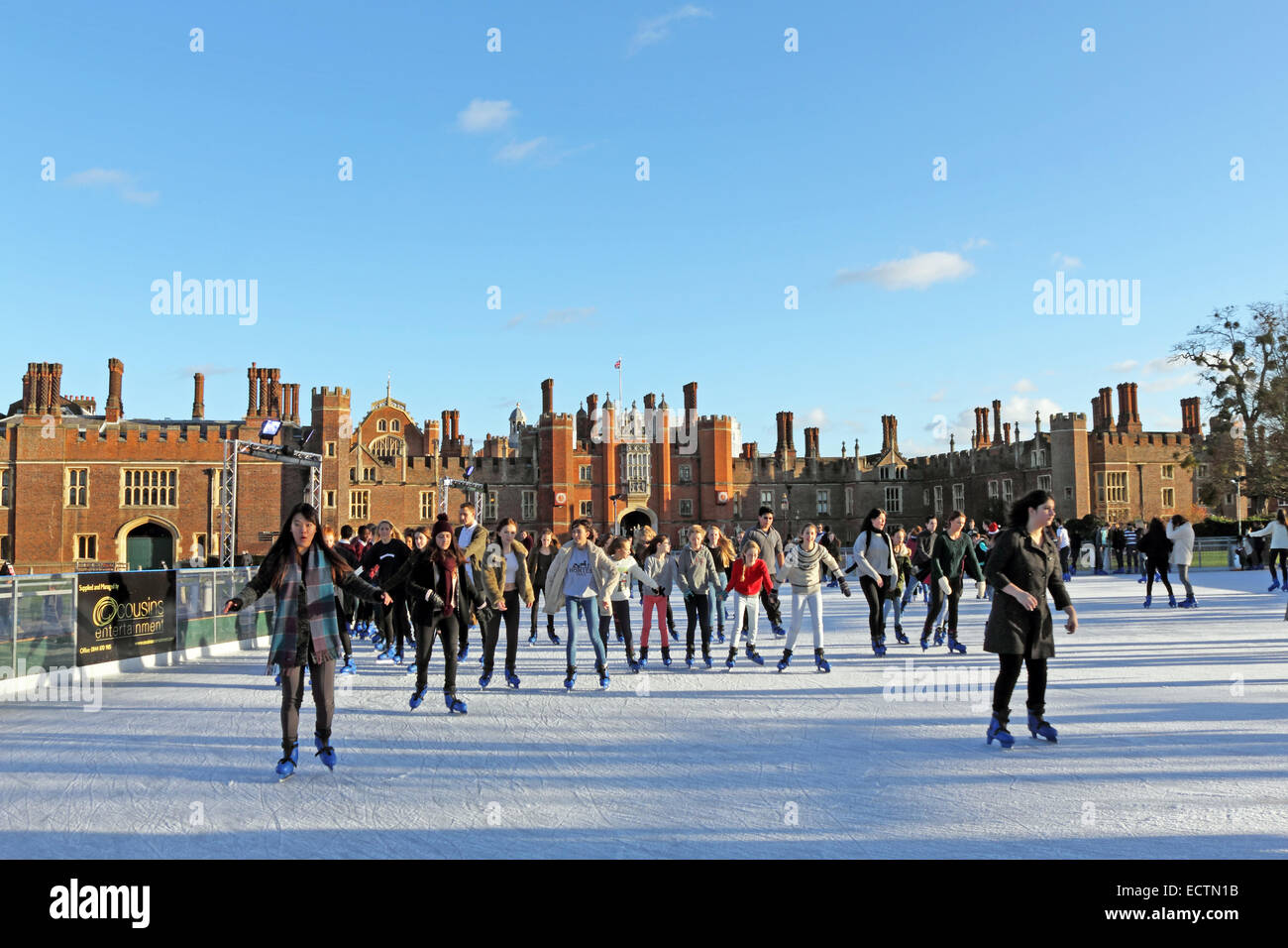 Hampton Court, SW London, England UK. 19th December 2014. On chilly but sunny day in SW London, friends, families and school parties enjoy festive fun at the Ice Rink in the grounds of Hampton Court Palace. It is a magical setting, surrounded by the Tudor Palace of Henry VIII, the River Thames and the gardens of Hampton Court. Stock Photo