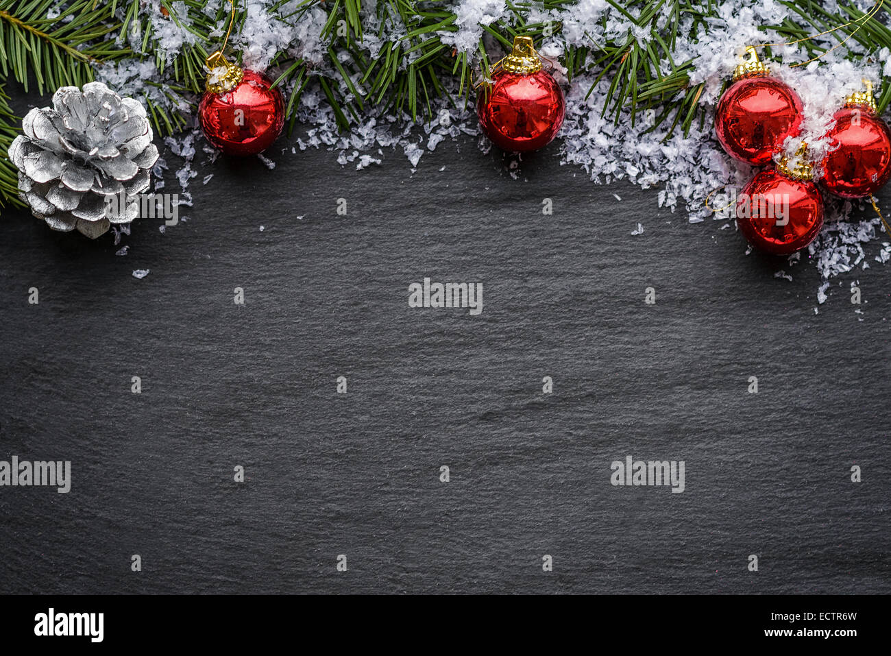 Christmas background with colorful red baubles, a silver decorative pine cone and green pine branches over a textured grey backg Stock Photo