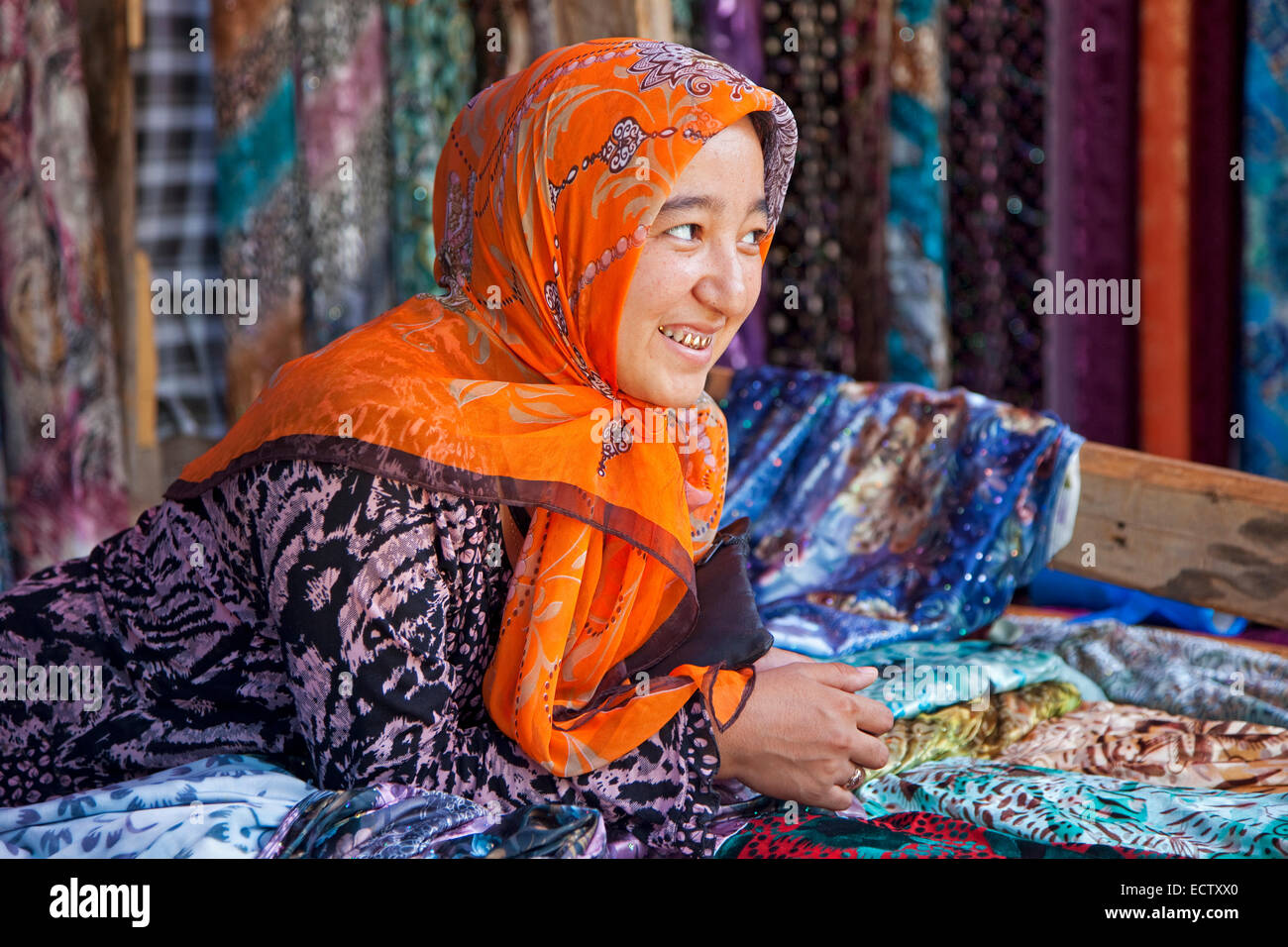 Kyrgyz woman with golden teeth selling colourful fabrics at market in Osh, Kyrgyzstan Stock Photo