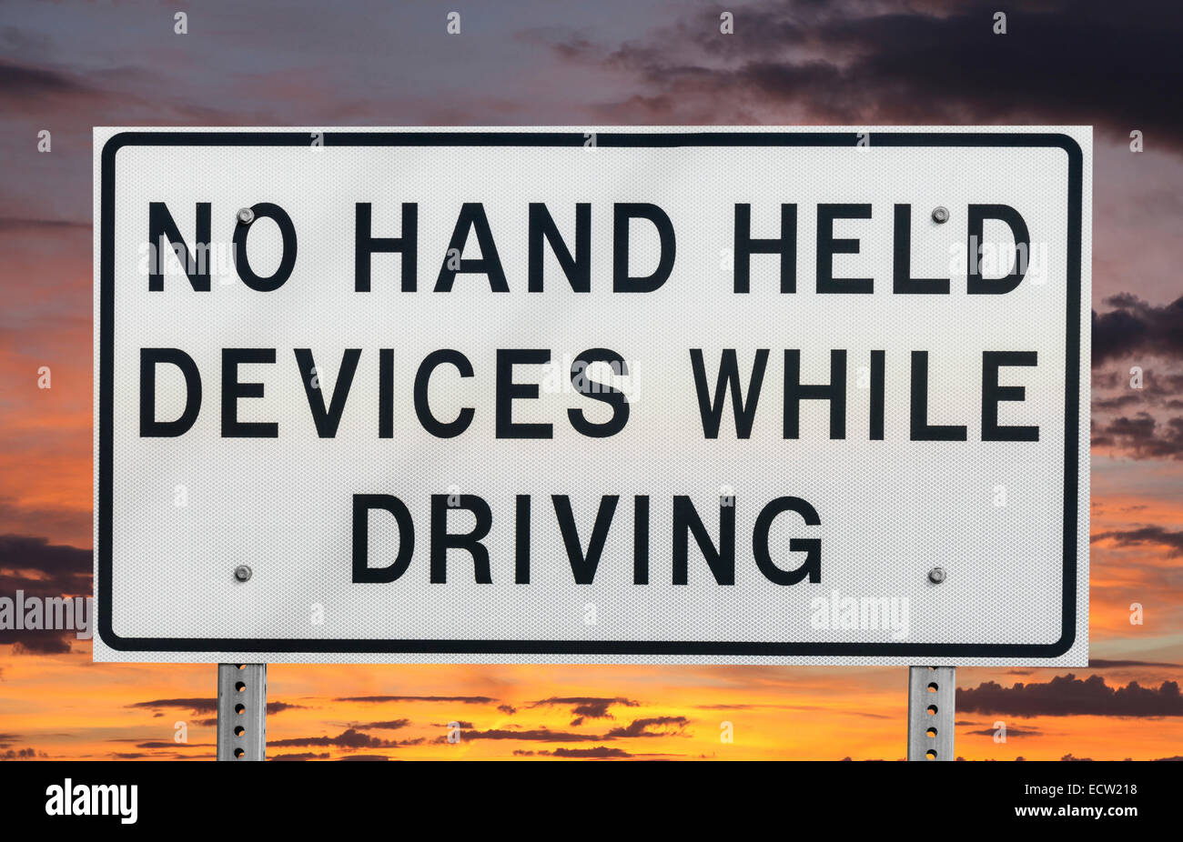No hand held devices while driving sign isolated with sunset sky. Stock Photo