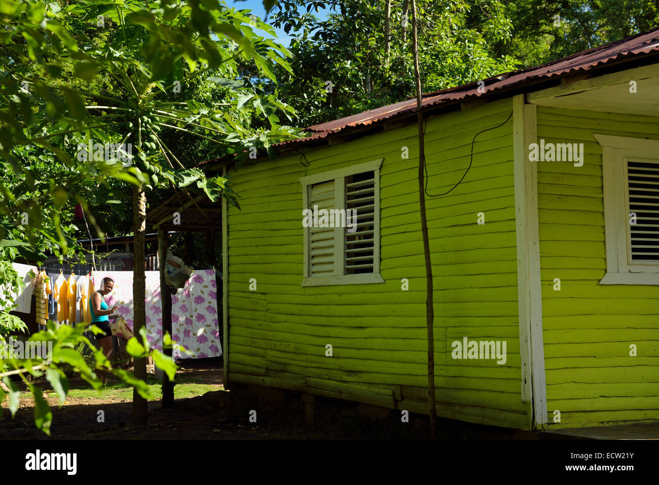 Laughing woman hanging out the clothes in the backyard of a green wood house Dominican Republic Stock Photo