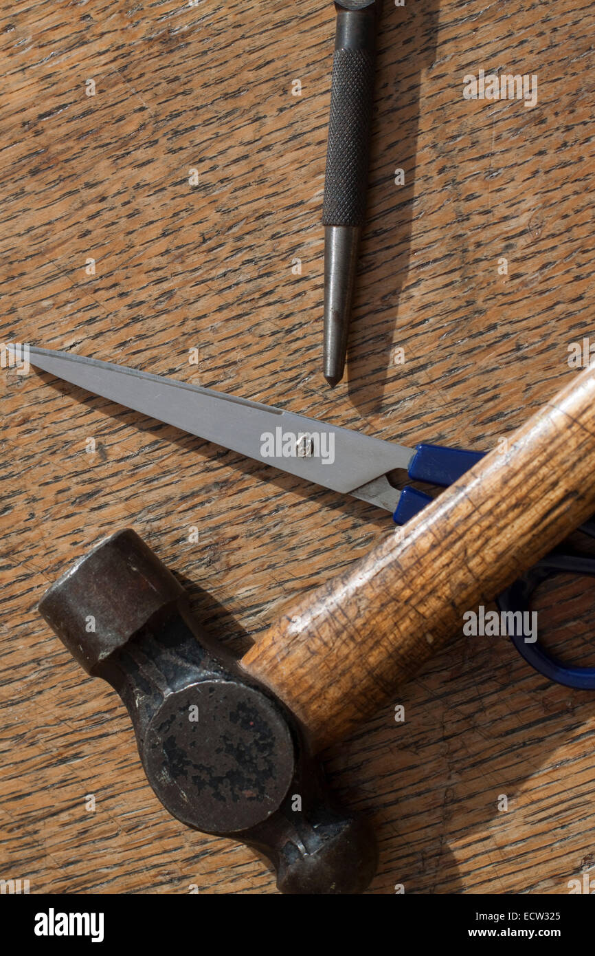 Ball pein/peen hammer, centre/center punch and blue handled scissors on a grained wooden surface