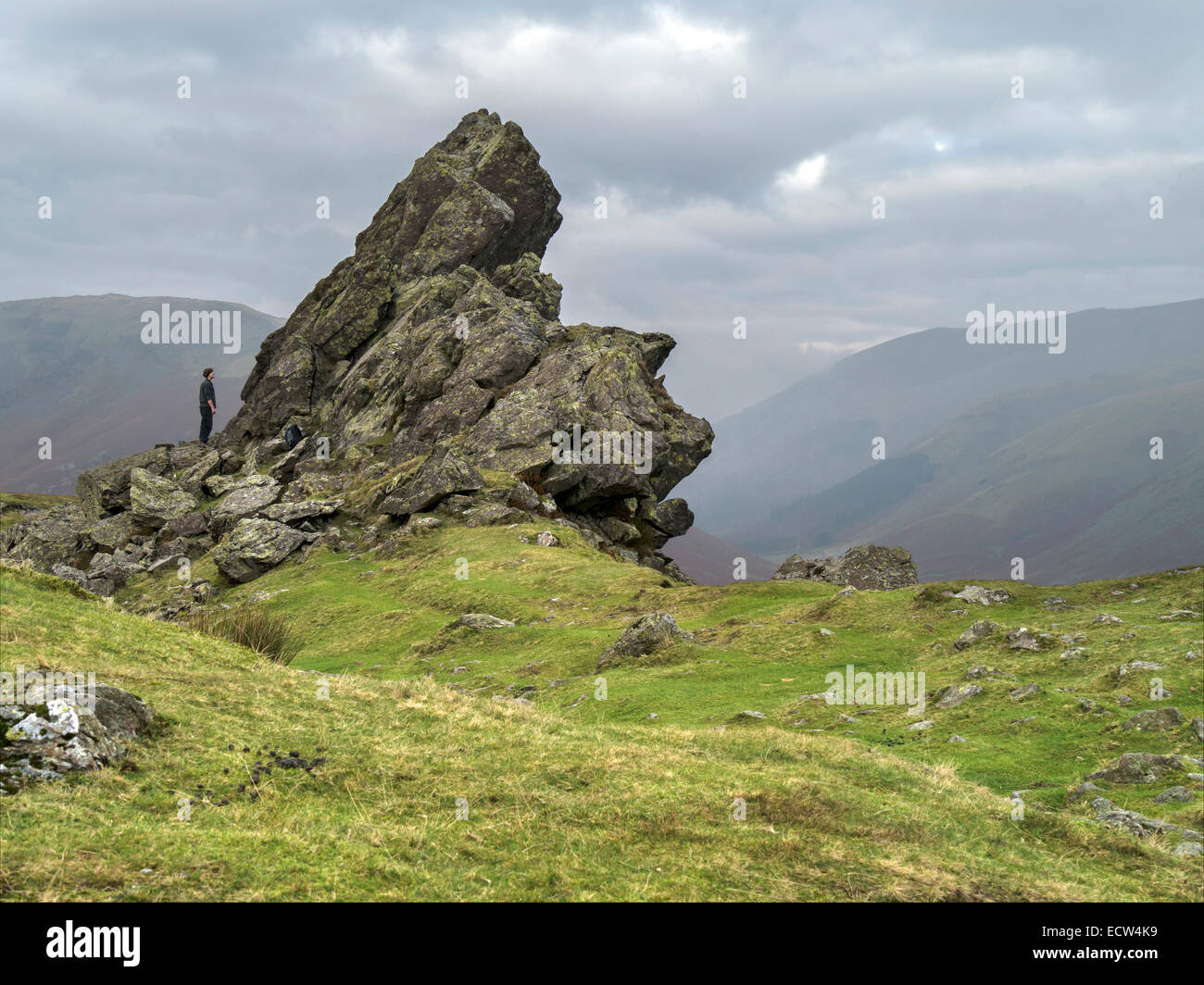 Hill walker admires 'Howitzer' rock formation on the summit of Helm Crag, Grasmere, Lake District, Cumbria, England, UK. Stock Photo