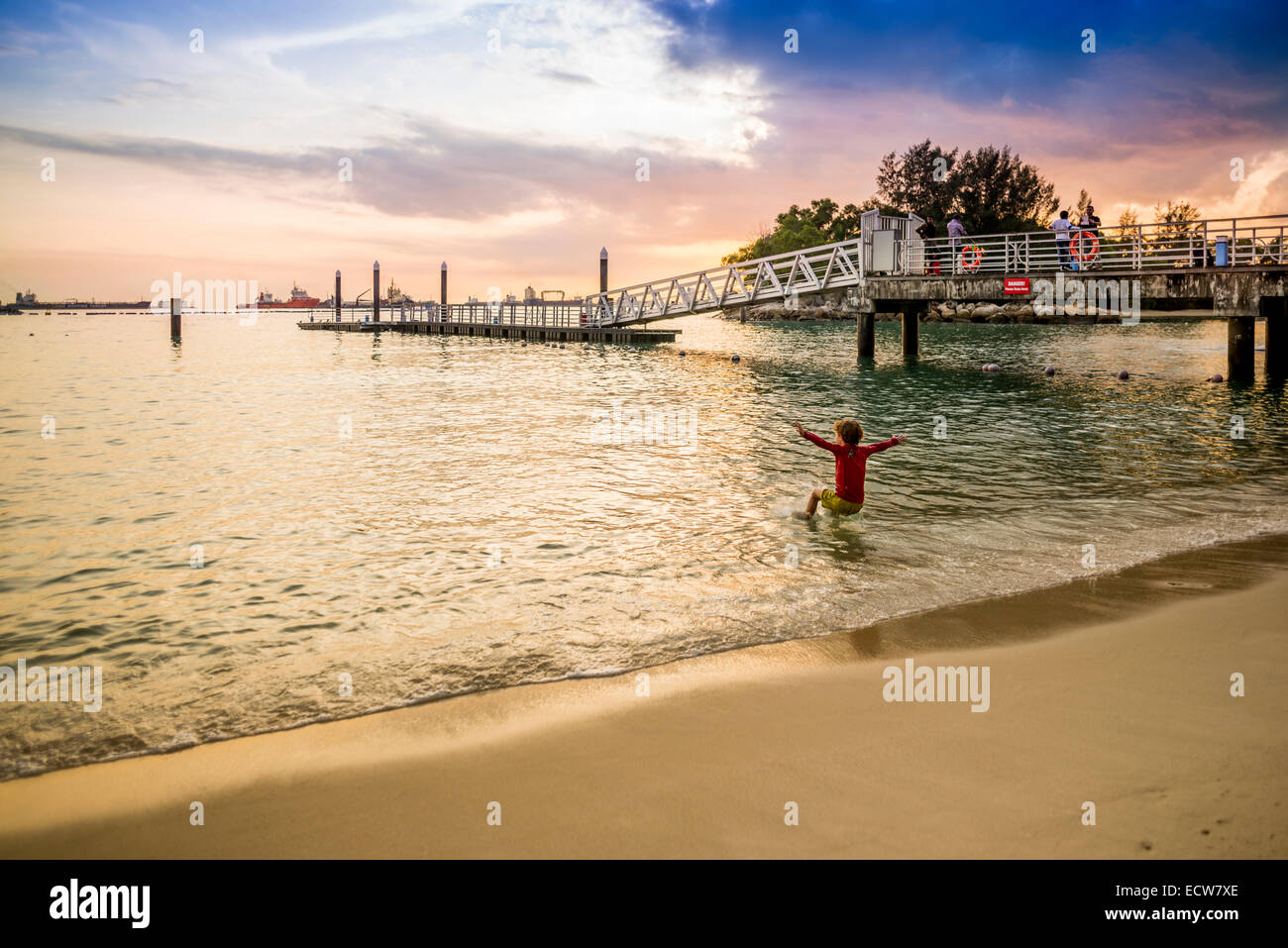 Kid jumping into the sea at Sentosa on a colorful evening sunset. Stock Photo