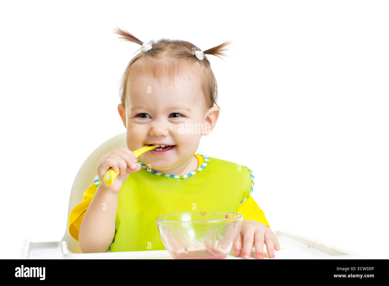 Happy baby eating with spoon sitting at table Stock Photo