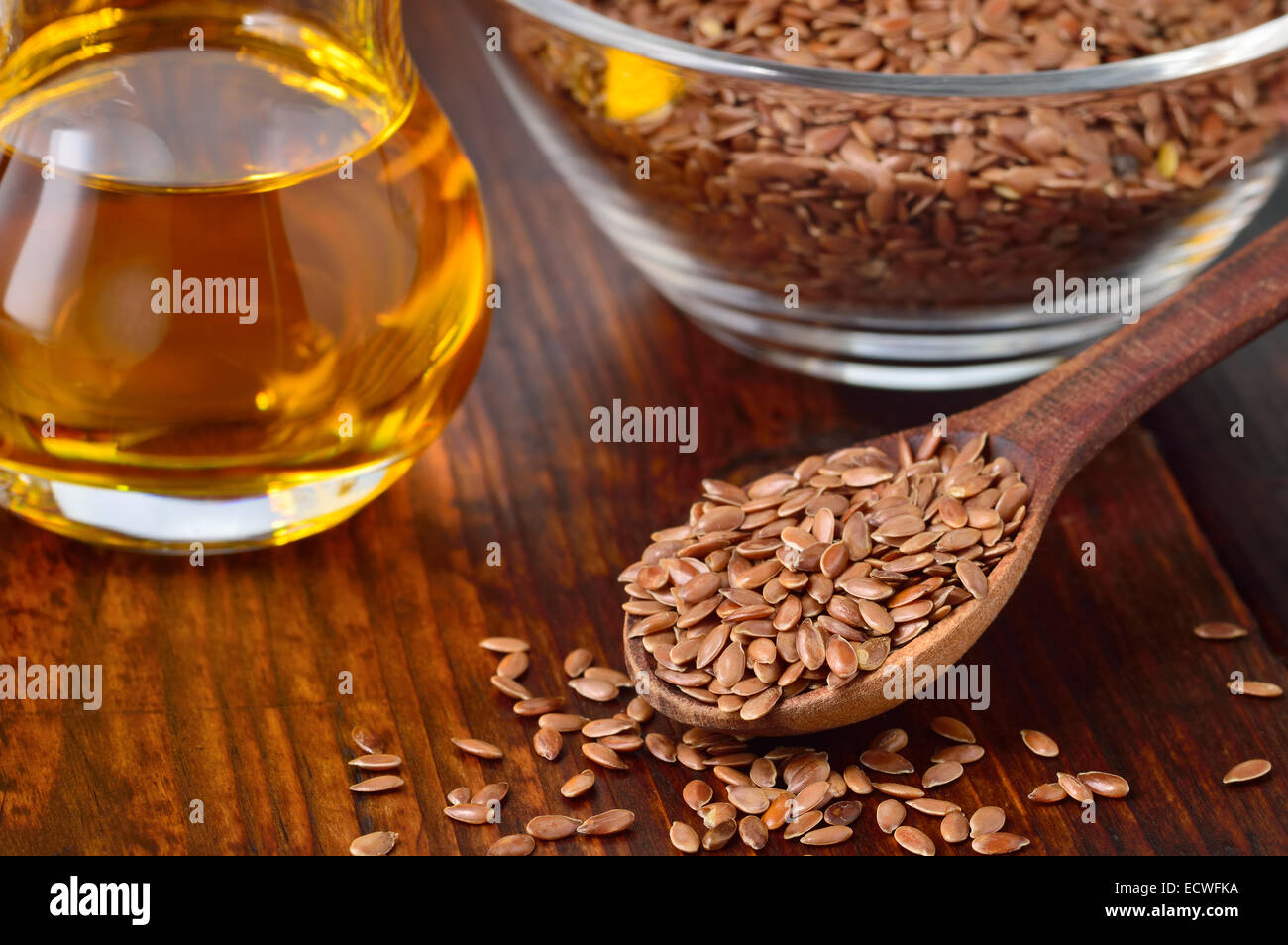 Brown flax seeds on spoon and flaxseed oil in glass jug on wooden table