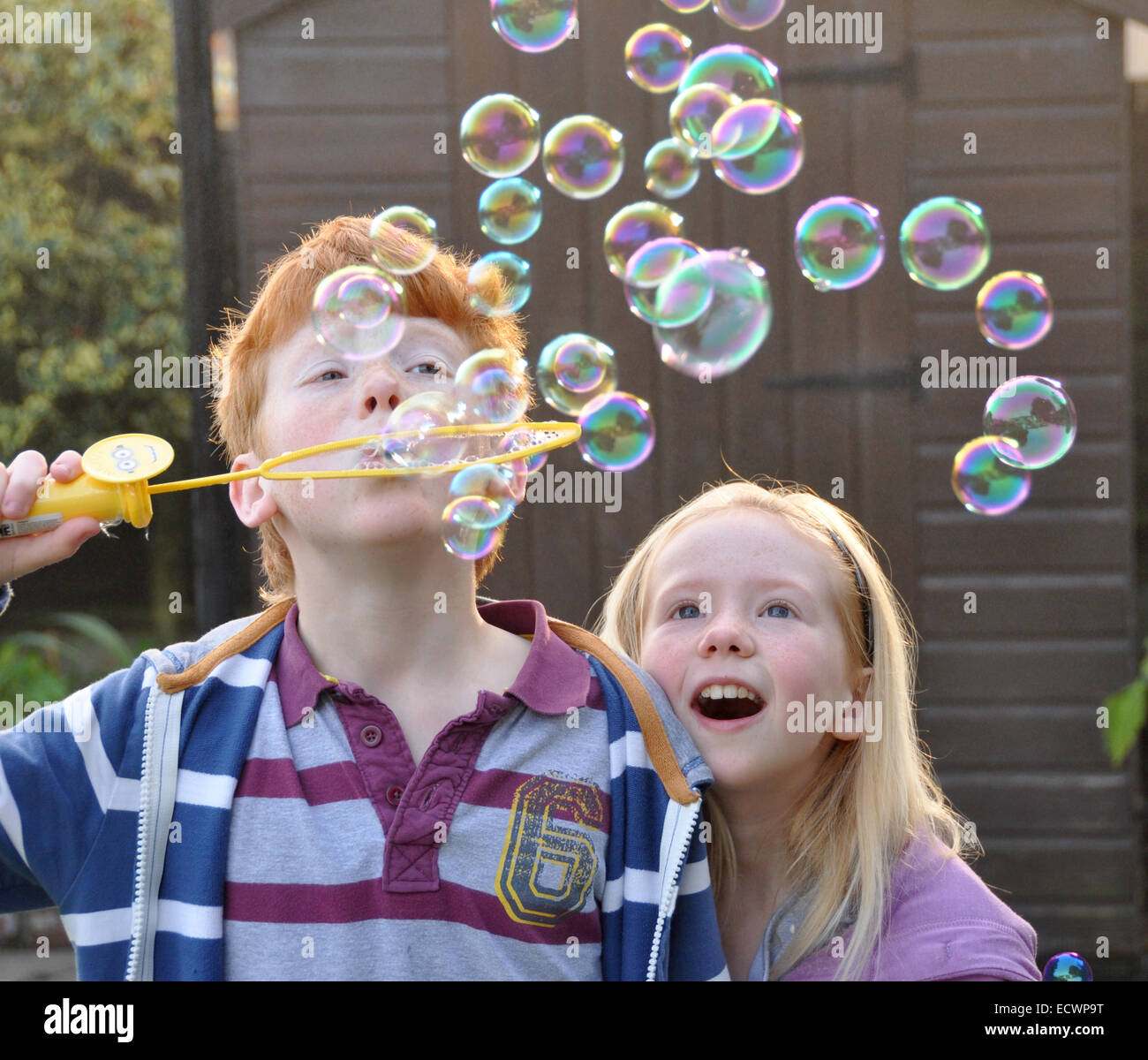 Children blowing bubbles; ginger haired boy with young sister Stock Photo