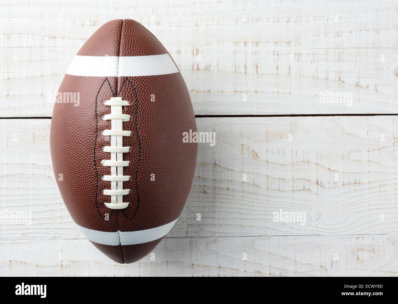 Closeup overhead shot of an American collegiate style football on a whitewashed wood table. The ball is offset ot the left with Stock Photo