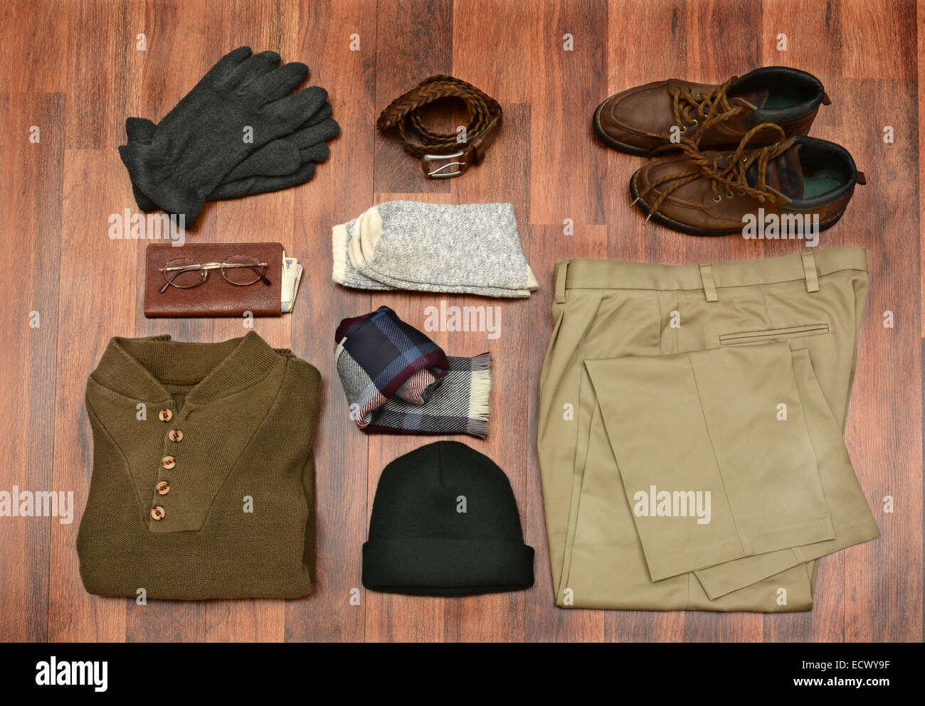 High angle shot of men's winter clothes laid out on a dark wood floor. Items include, Sweater, Scarf, Gloves, wool Socks, Pants, Stock Photo