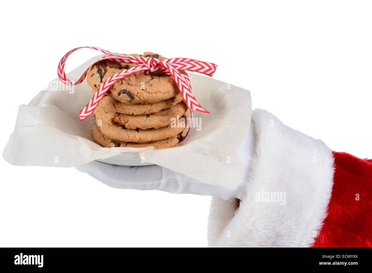 Santa Claus holding a plate with a stack of chocolate chip cookies tied with a ribbon. Only Santa's gloved hand and red sleeve a Stock Photo