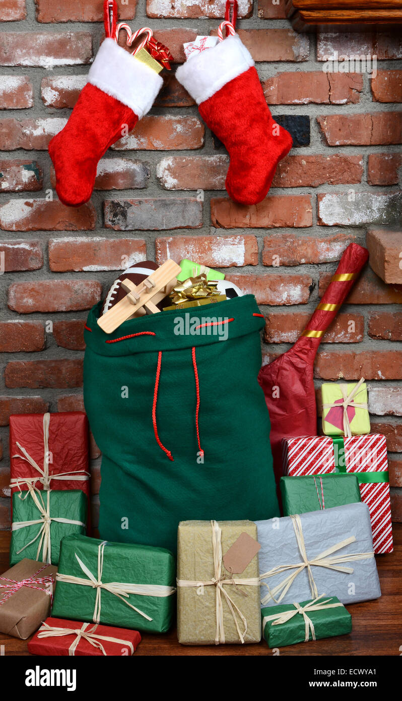 Santa Claus' bag leaning on the bricks of a hearth. The bag is stuffed with toys and surrounded by wrapped presents. Stock Photo