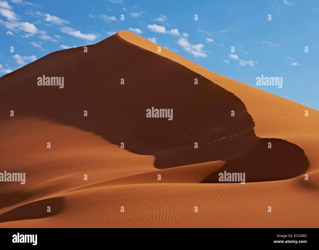 View of sand dunes in desert with blue sky and clouds in background ...