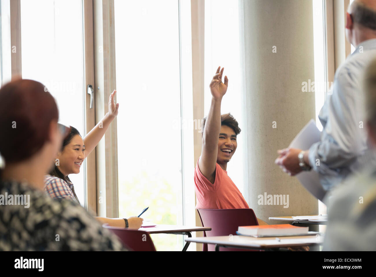Smiling university students raising hands at seminar Stock Photo