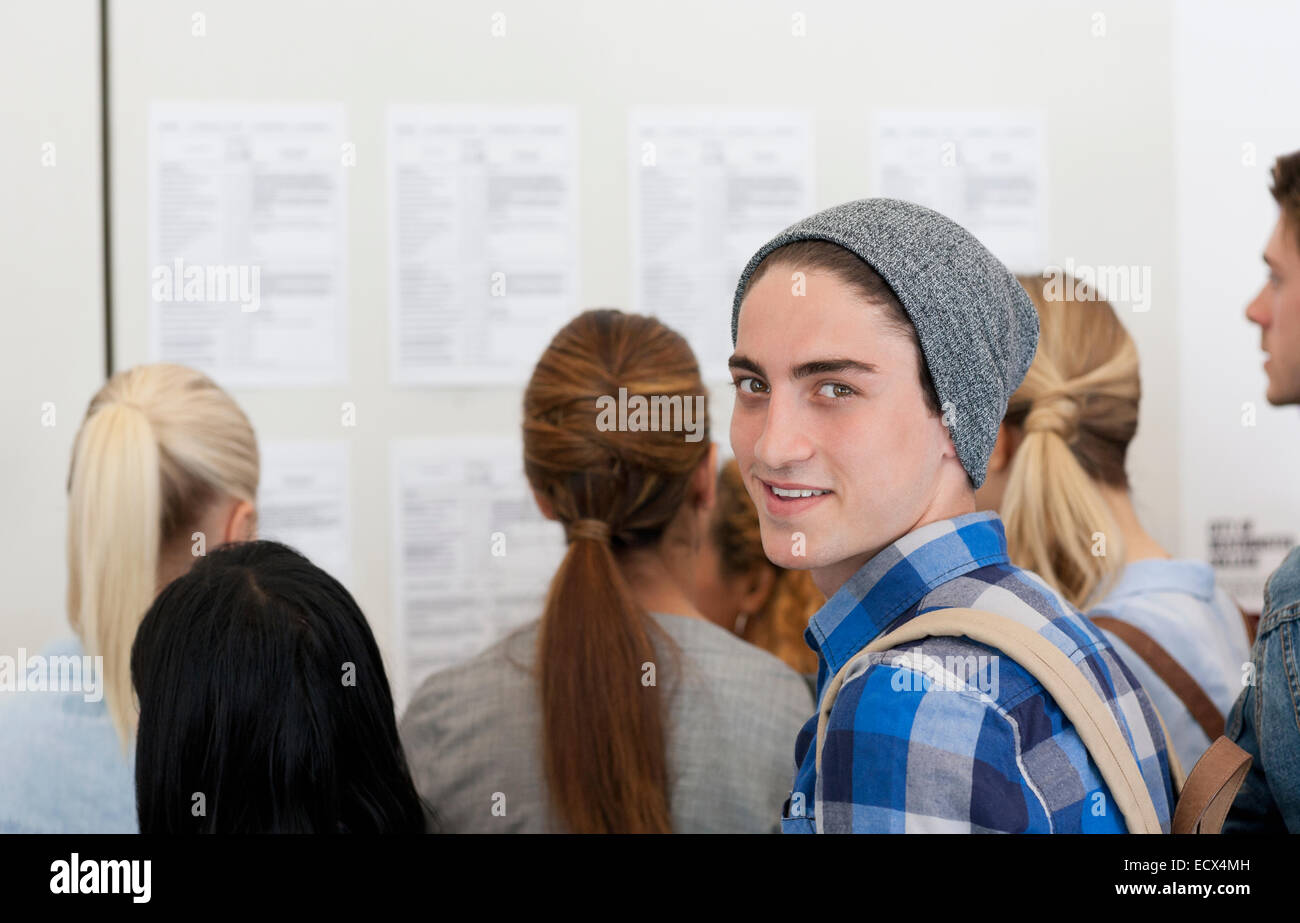 Male student smiling at camera while others read notice board Stock Photo