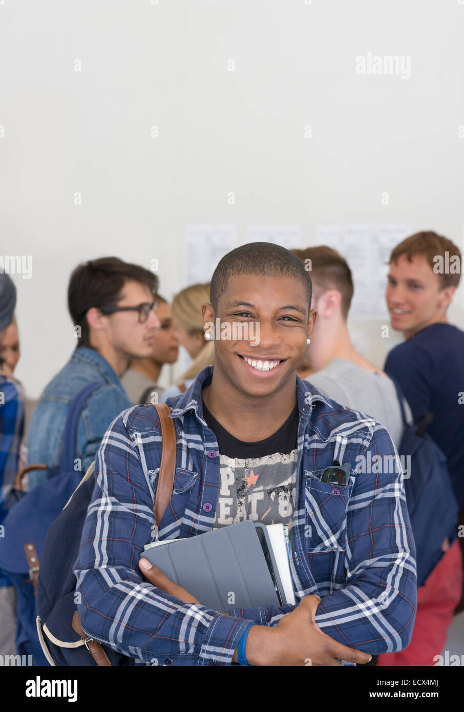 Male student holding books and smiling at camera with other students in ...