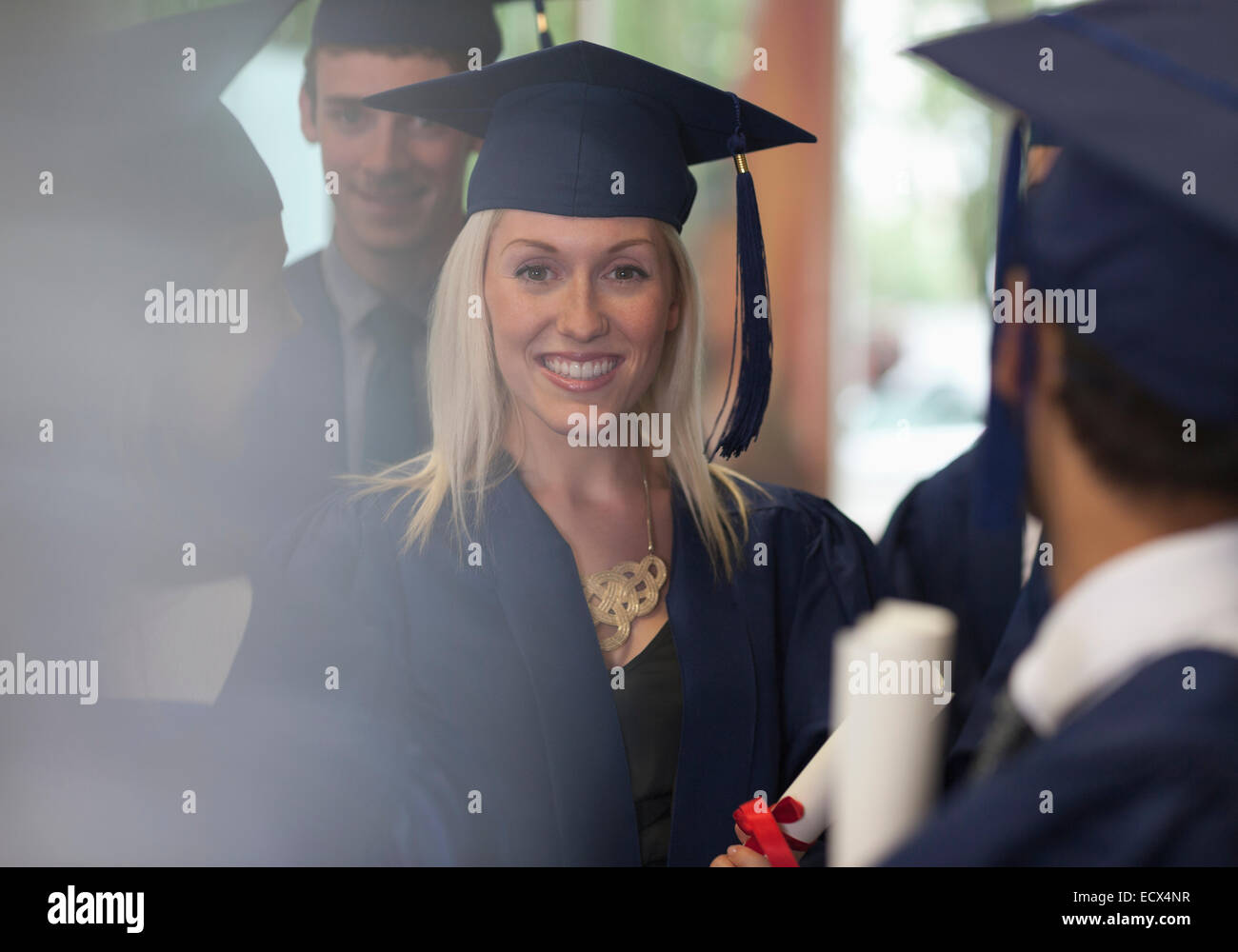 Female student smiling in graduation clothes surrounded by other students Stock Photo