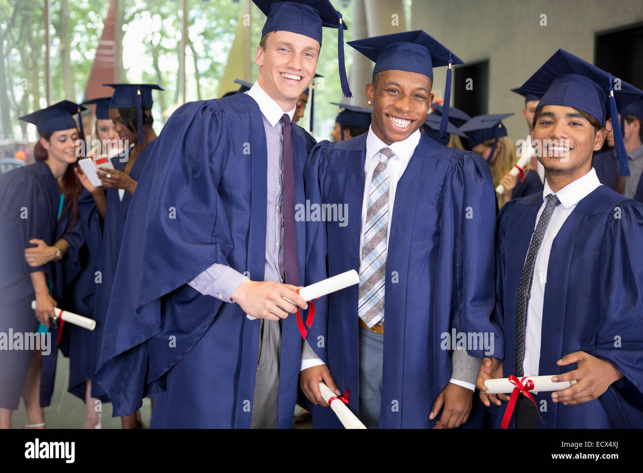 Portrait of three smiling male students in graduation gowns holding diplomas Stock Photo
